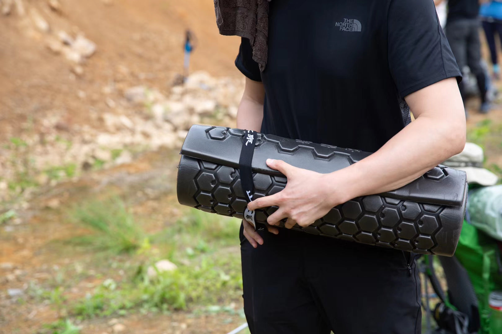 A person wearing a North Face short-sleeved shirt is holding a Mountain Spring black roll-up foam pad.